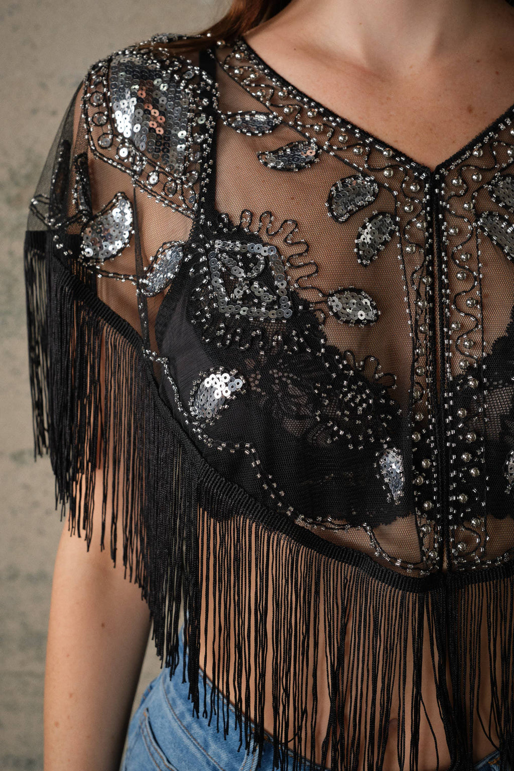 Sheer black mesh cape with intricate sequin and bead embellishments, featuring dramatic fringe trim and an open front.
