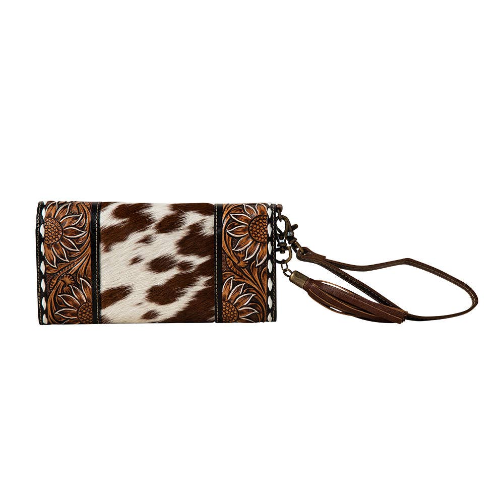 Hand-tooled wristlet wallet in brown and white cowhide, featuring floral designs and a leather wrist strap.