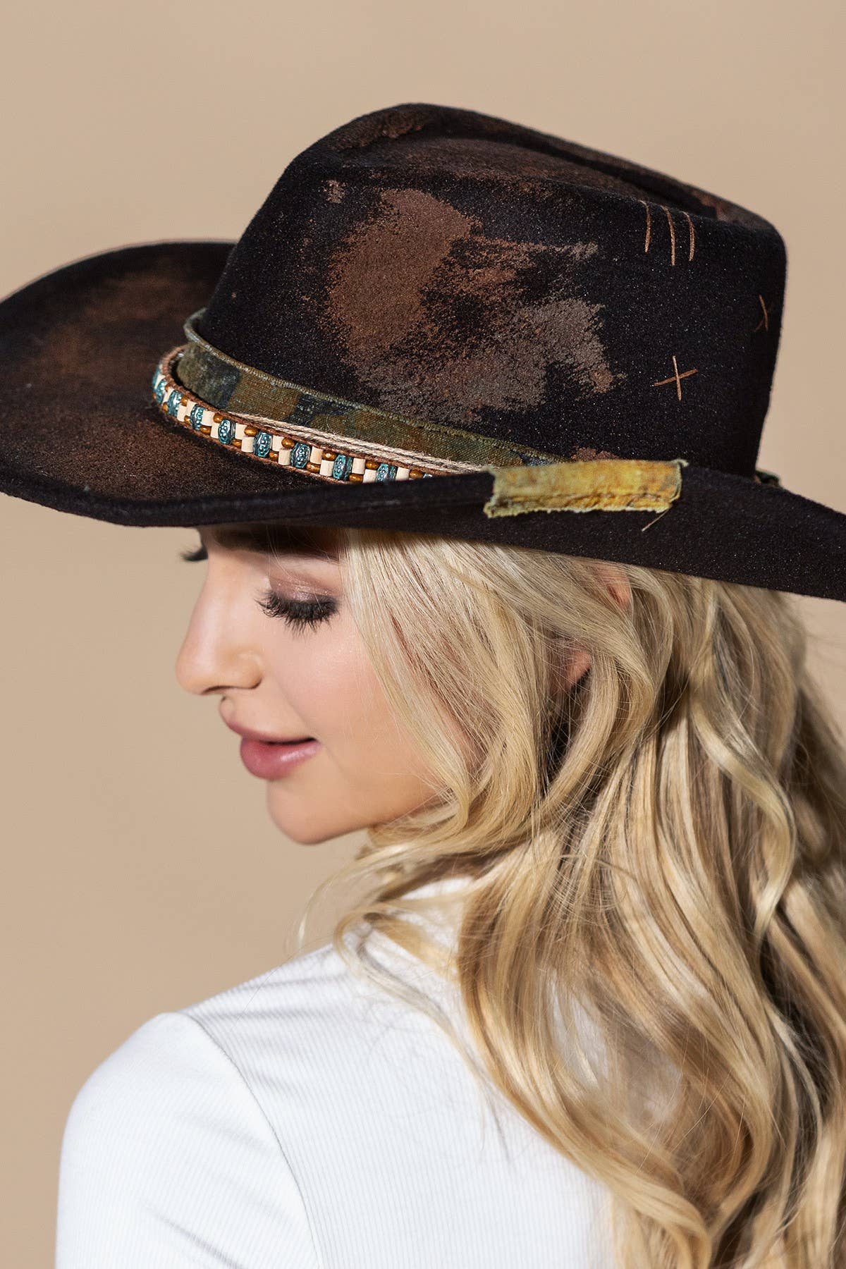 Distressed black vintage cowgirl hat with a beaded turquoise band, styled on a model with long, wavy hair.