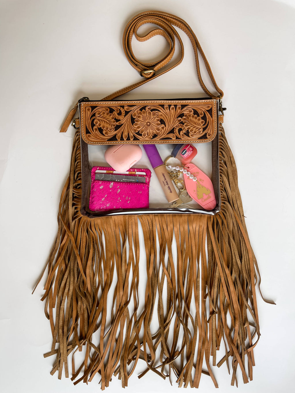 Boho-style clear crossbody purse with hand-tooled leather and fringe detail, featuring a secure snap closure and adjustable strap.