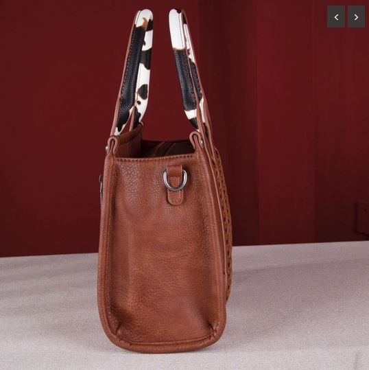 Brown simulated leather tote with cow print handles, whipstitch detailing, and a top zipper closure.