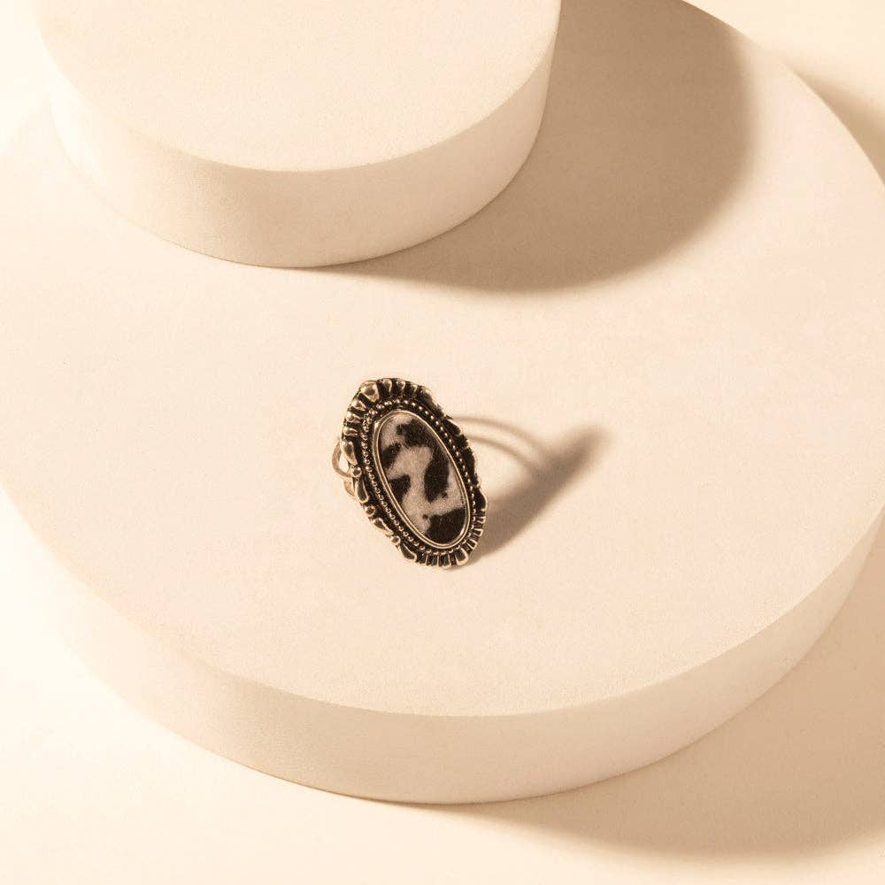 Adjustable Myra Outlaw Hide ring featuring a black and white cowhide pattern set in a textured zinc alloy frame.