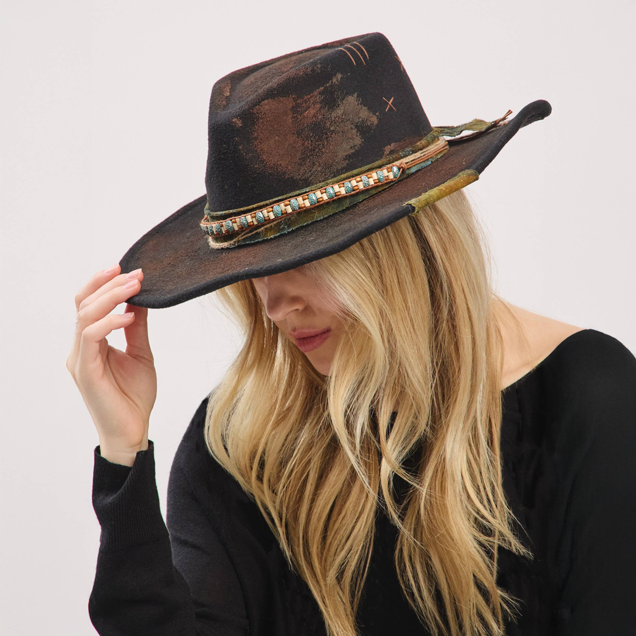 Rustic shapeable cowgirl fedora hat with a distressed fabric band and decorative beads, worn tilted on a model's head.