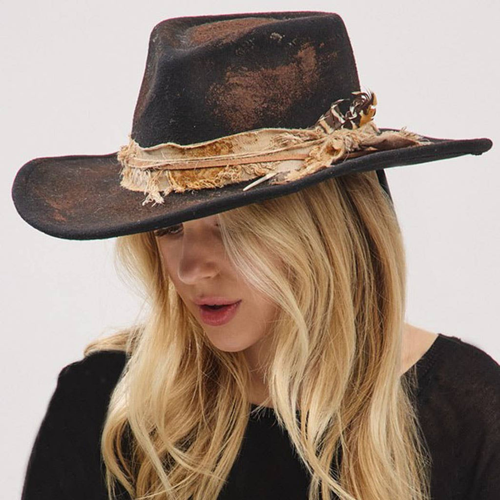 Vintage versatile shapeable cowgirl and fedora hat with feather and distressed fabric band worn by woman