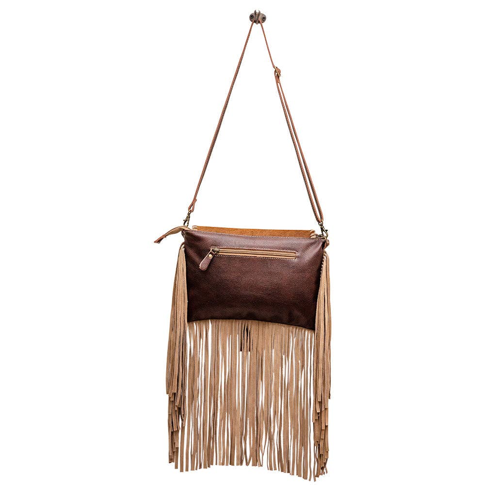 Brown leather and hair-on hide bag with tan fringe detail, featuring a front zip pocket and adjustable shoulder strap.