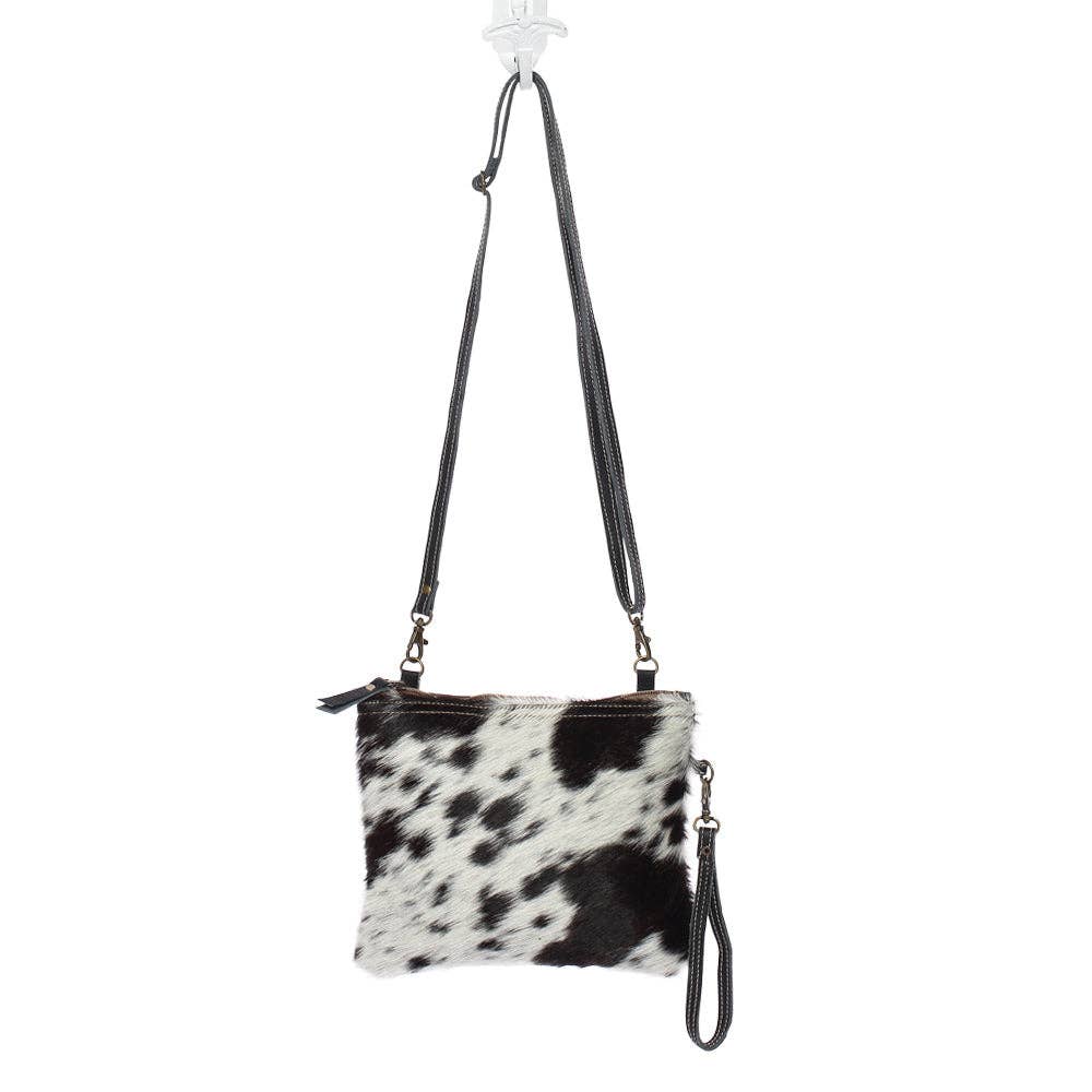 Cowhide crossbody bag with bold black and white pattern, featuring leather straps and a zippered closure.