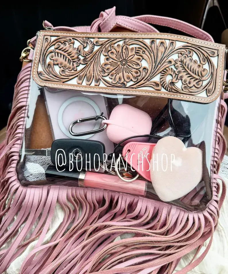 Clear crossbody purse featuring a floral tooled leather flap, pink fringe, and visible accessories inside.