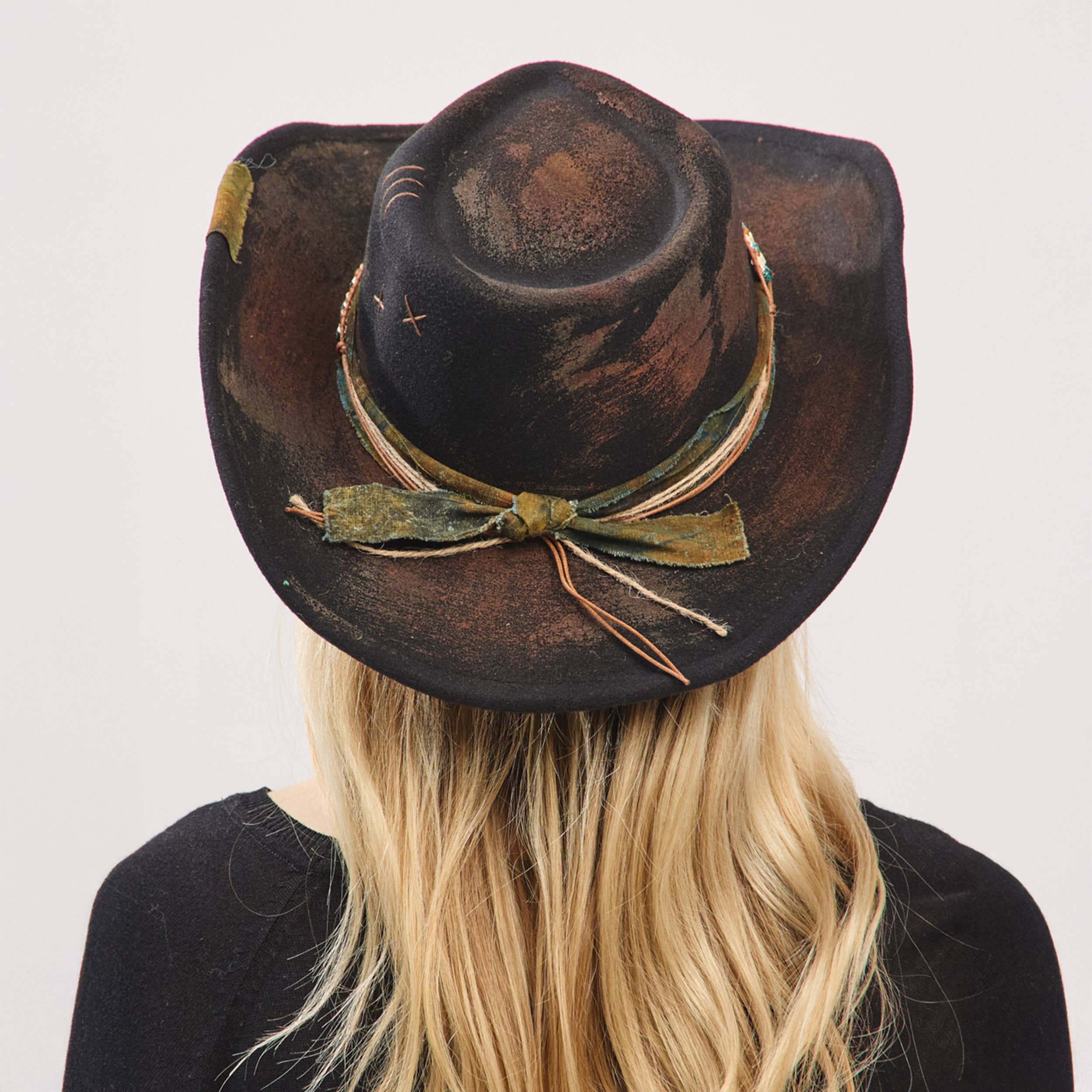 Distressed black cowgirl fedora hat with a rustic fabric band and shapeable brim, worn by a model with long hair.