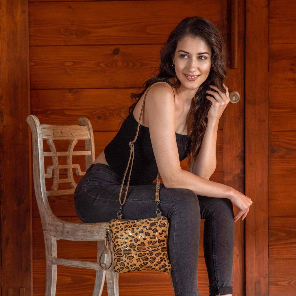 Leopard print hairon and leather bag with gold specks, worn on a shoulder strap by a model in a black top and jeans.