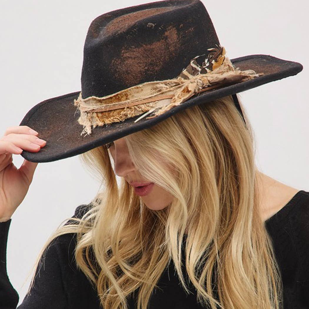 Woman wearing vintage cowgirl and fedora hat with feather and distressed fabric band