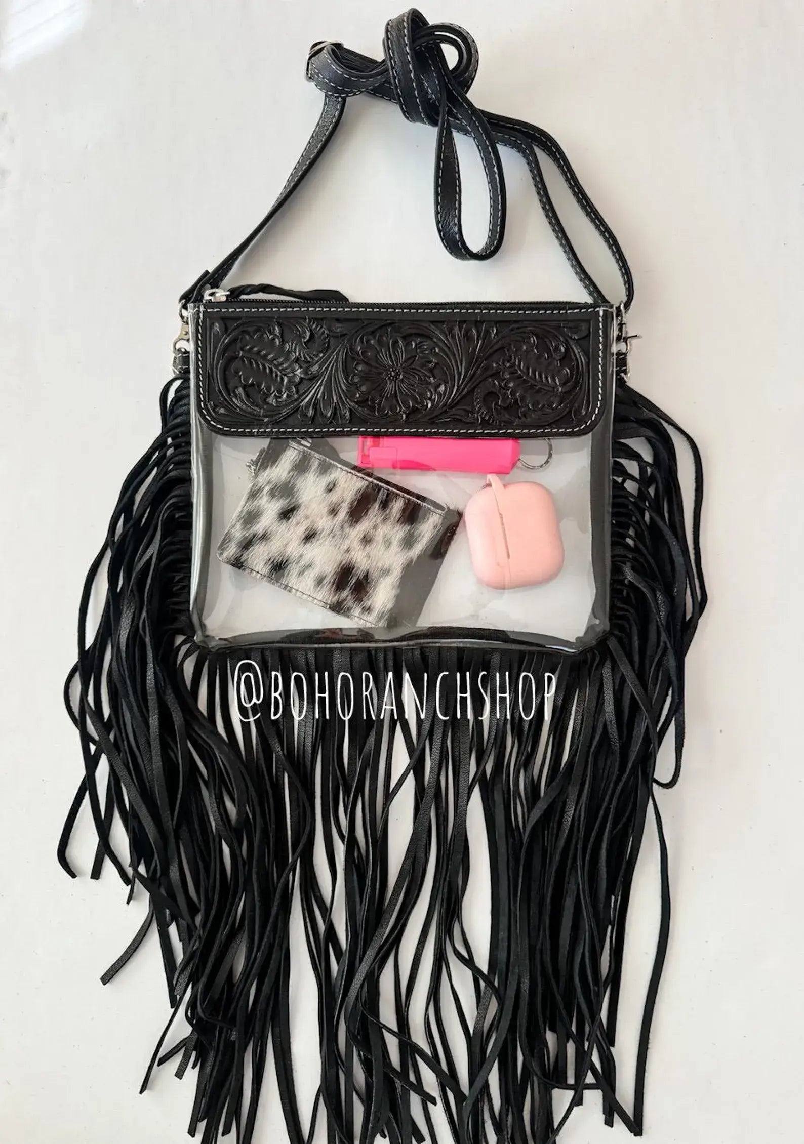 Clear crossbody purse with black fringe, featuring a decorative black leather top and transparent interior showcasing items.