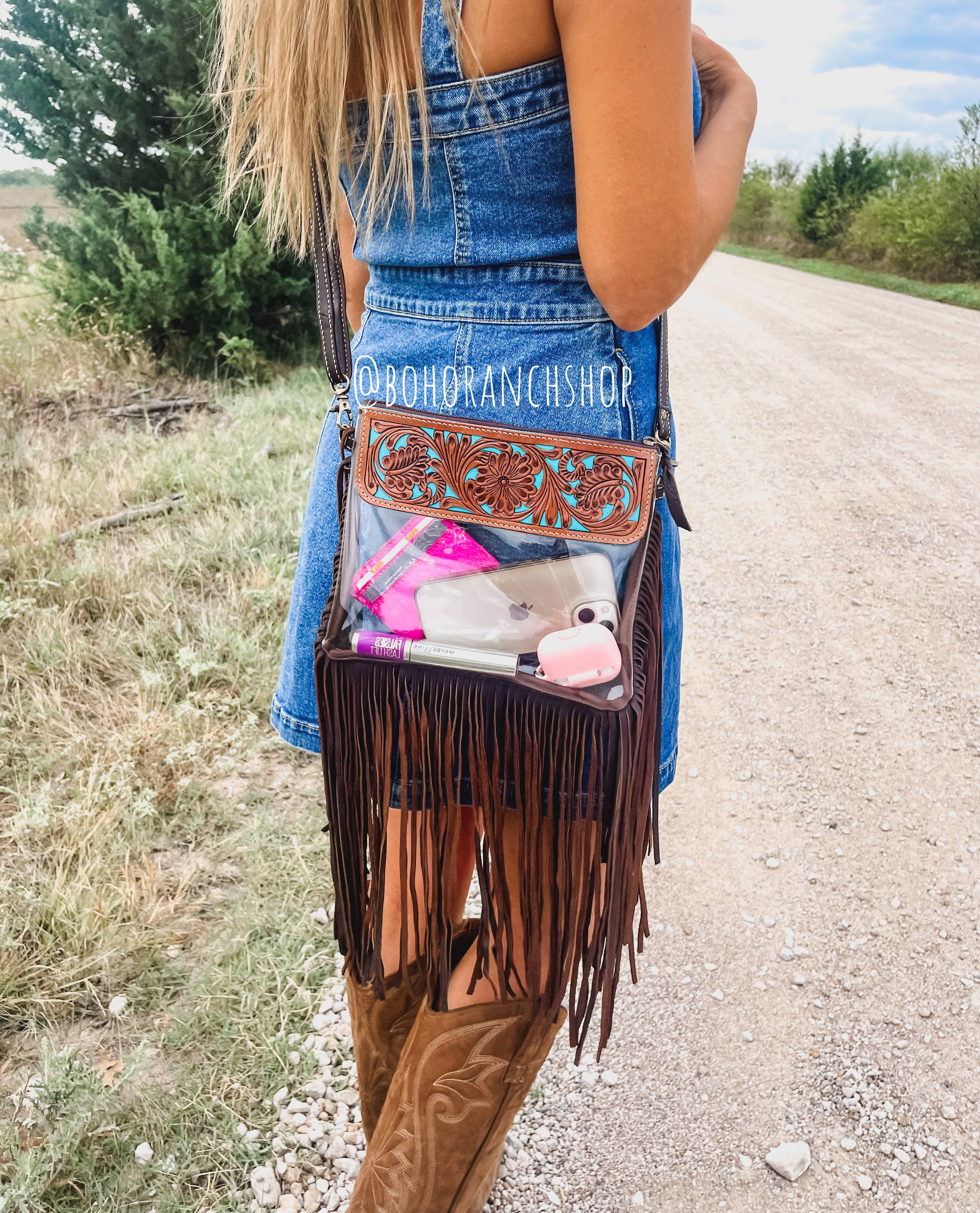 Clear crossbody bag with leather trim and fringe, worn with a denim dress, featuring a secure snap closure and adjustable strap.