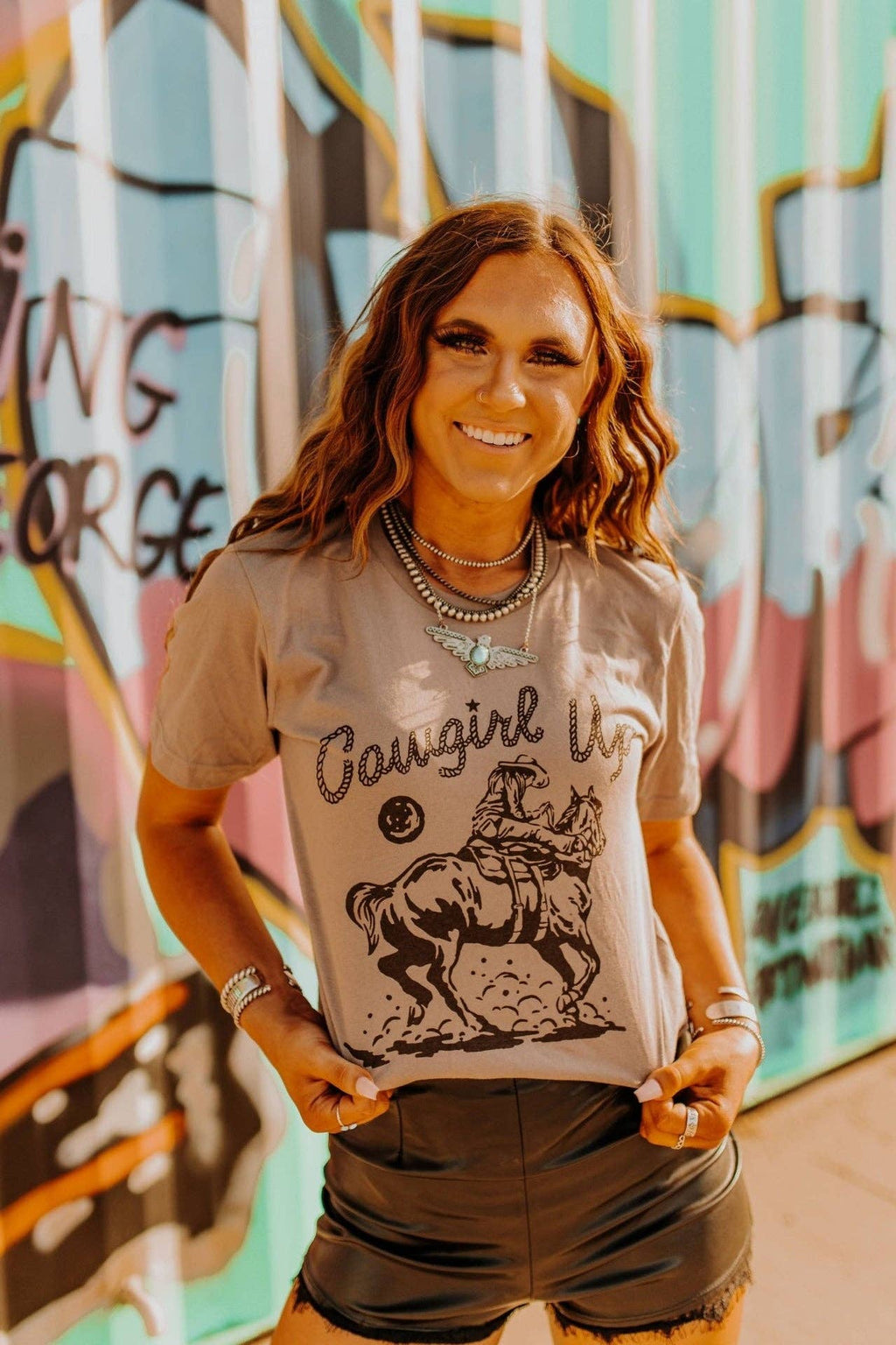 Woman wearing brown Cowgirl Up Graphic Tee with horse riding cowboy design in urban setting