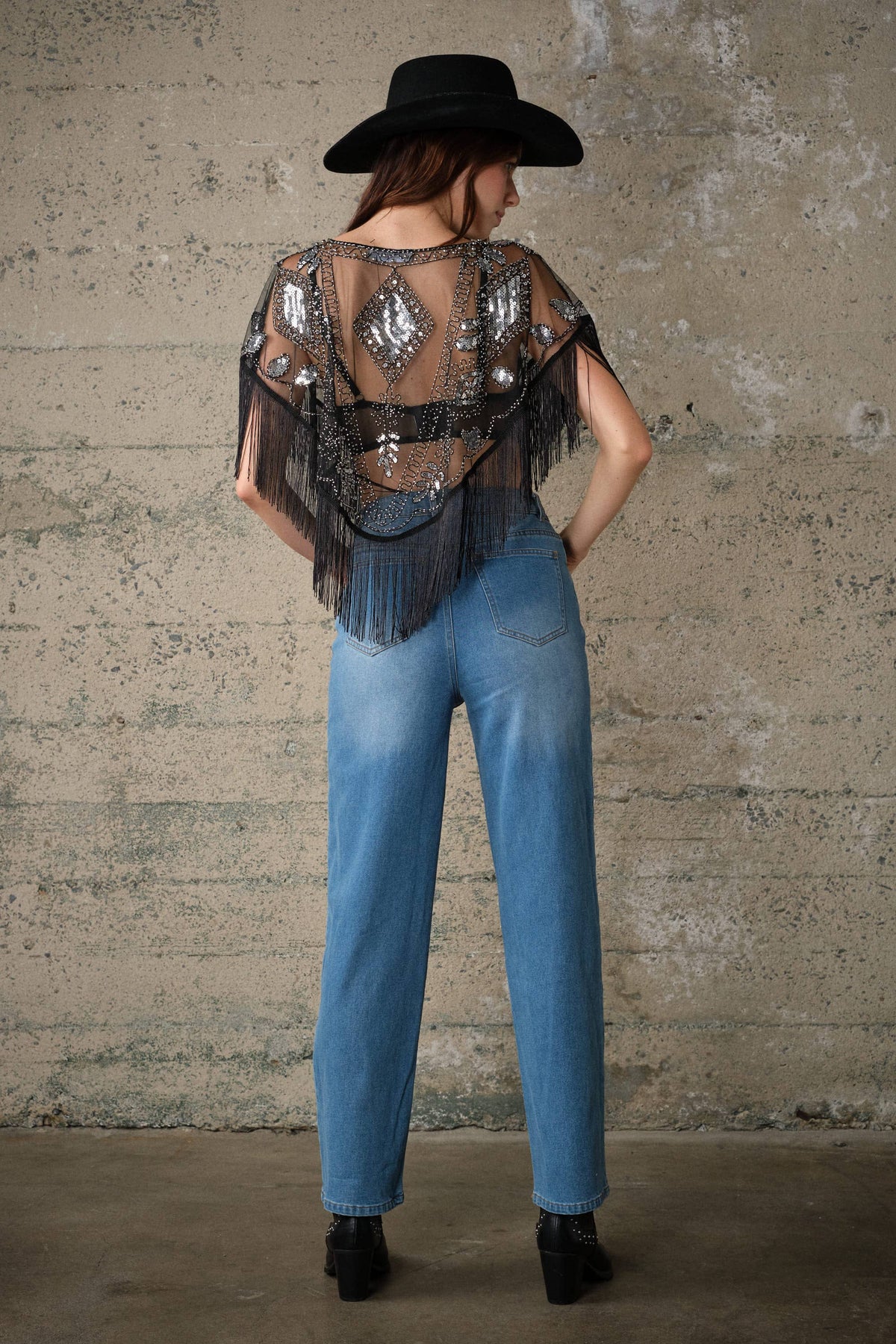 Sheer black mesh cape with sequins and beaded embellishments, dramatic fringe trim, open front, styled over high-waisted jeans.
