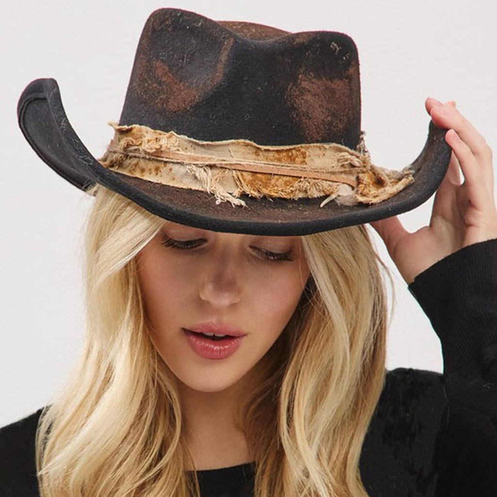 Woman wearing vintage cowgirl and fedora hat with distressed fabric band and feather accessory