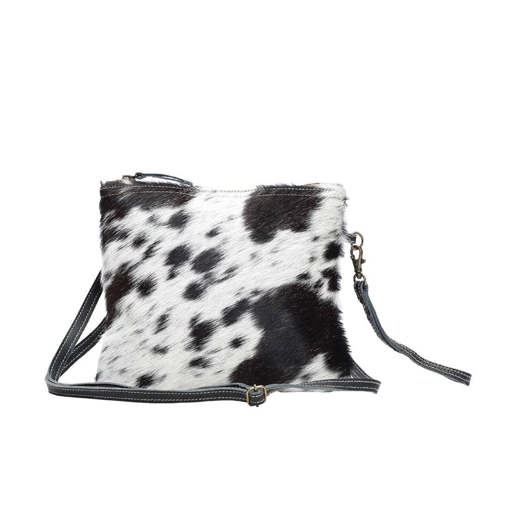 Black and white spotted cowhide bag with a zipper closure and adjustable crossbody strap. Casual and boho western style.
