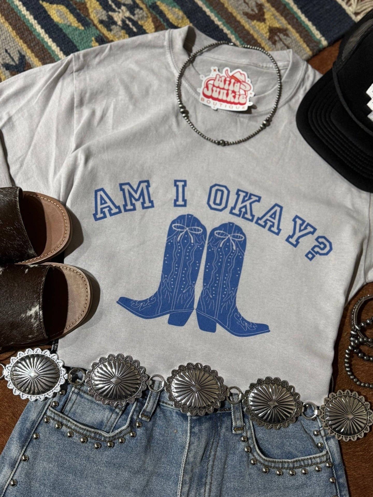 Am I Okay Graphic Tee with blue cowboy boots print, styled with studded denim shorts and silver concho belt.