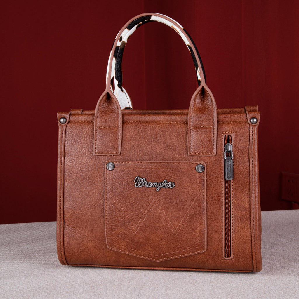 Brown simulated leather tote with cow print handles, whipstitch details, and Wrangler logo. Features a zippered back pocket.