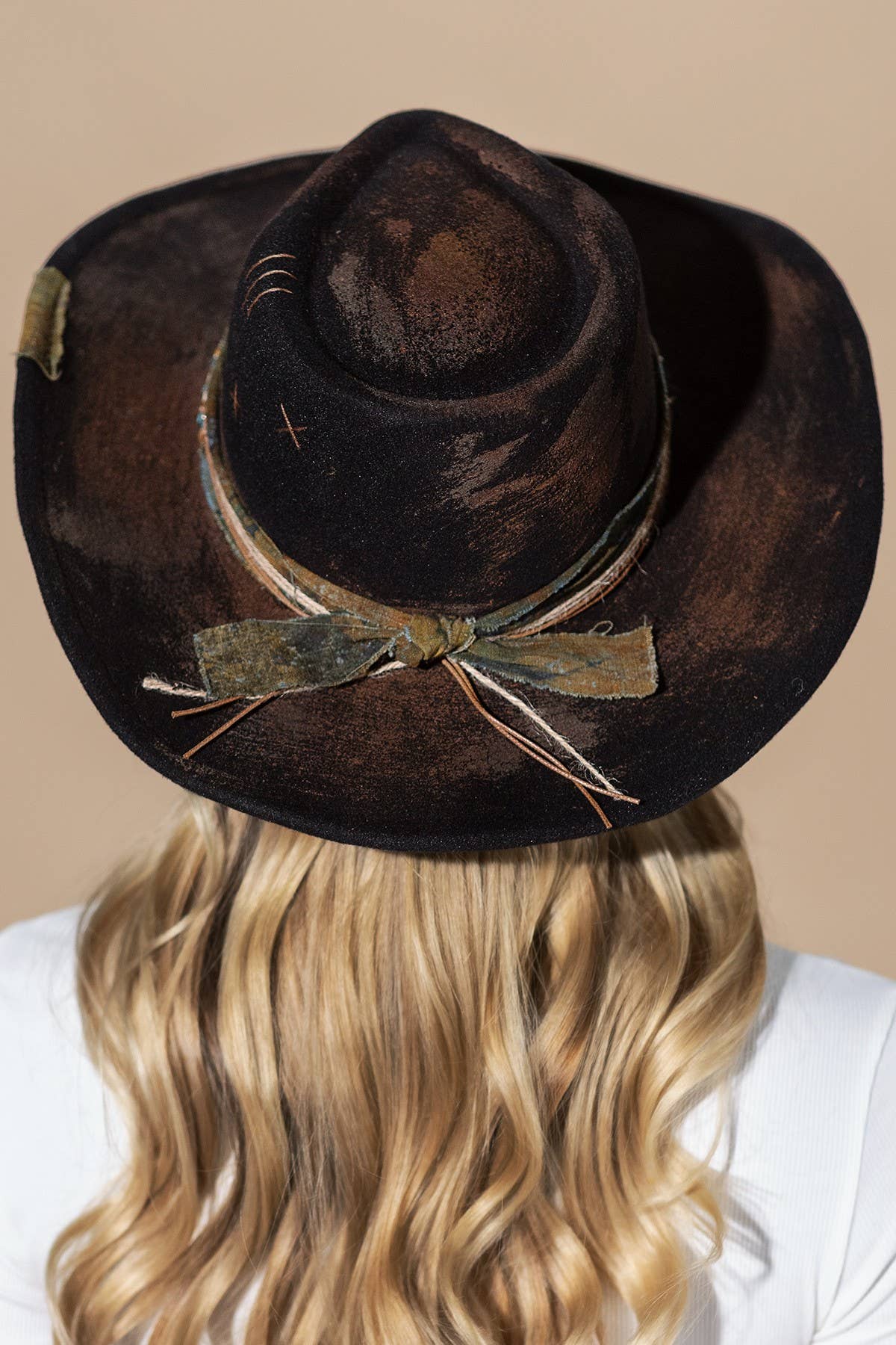 Distressed black wide-brim cowboy hat with a shapeable design, featuring a decorative fabric wrap and bow.