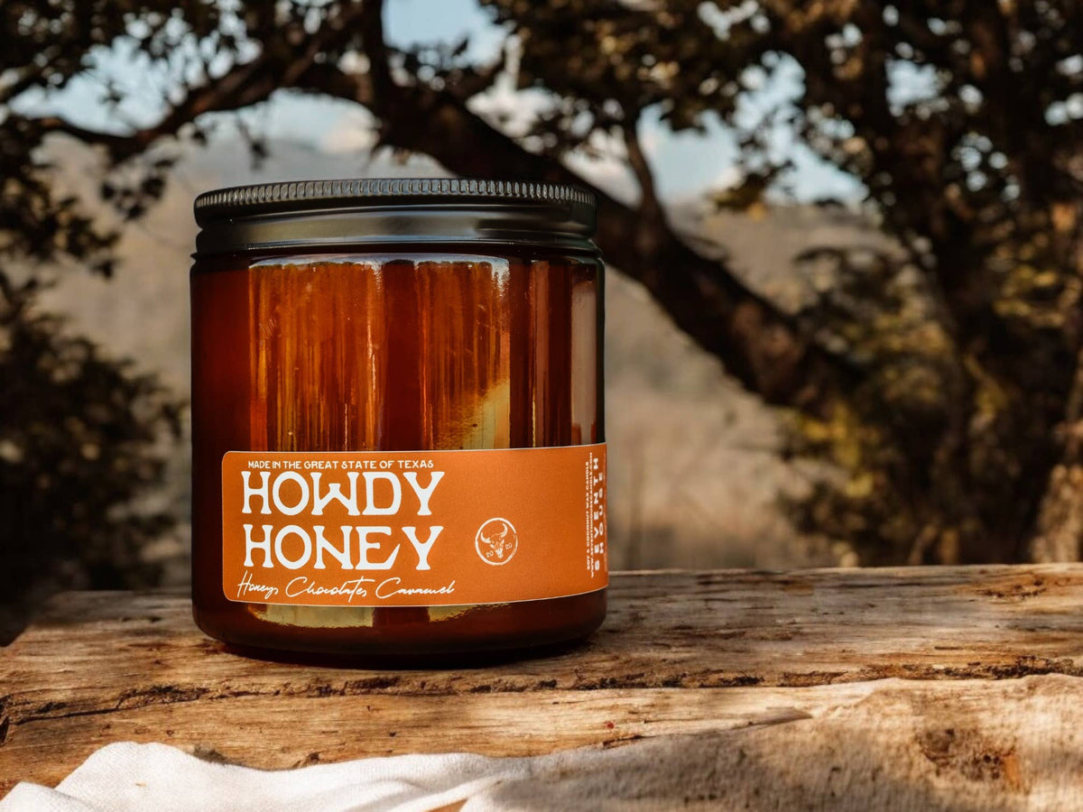 Howdy Honey amber jar candle with vanilla caramel and honey scent on rustic wooden surface outdoors