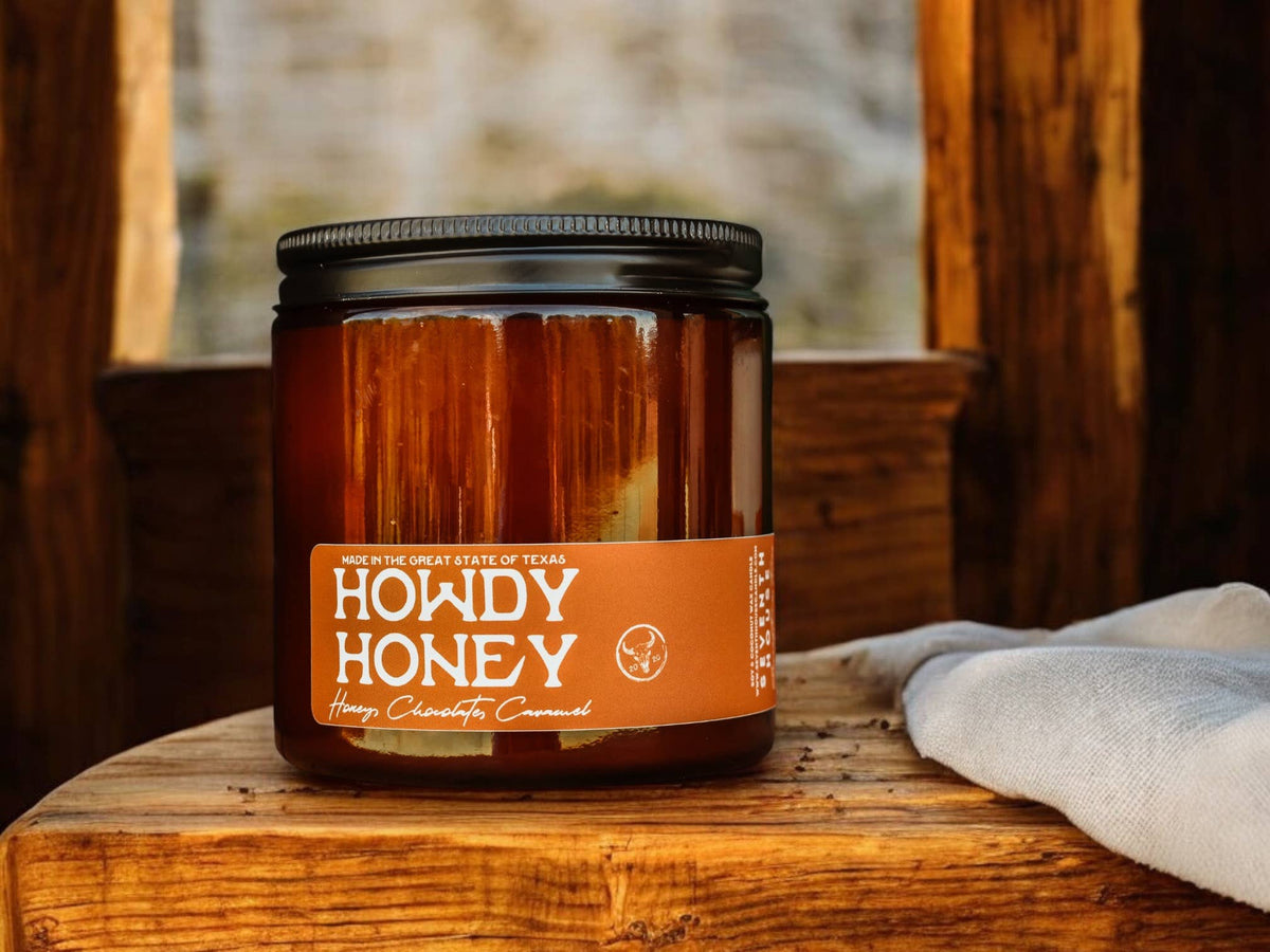 Howdy Honey vanilla caramel and honey scented amber jar candle with black lid on wooden surface