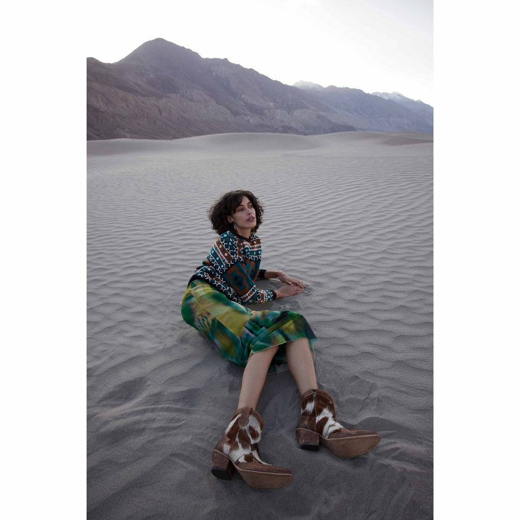 Western-style Georgia Trail hair-on hide and hand-tooled leather boots with snip toe, worn by a seated model in a patterned outfit.