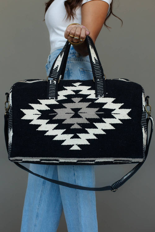 Black, white, and tan duffel bag featuring a geometric western pattern, with dual handles and an adjustable strap.