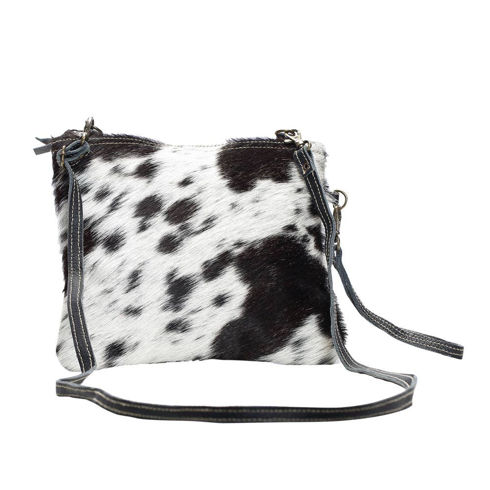 Black and white cowhide crossbody bag featuring a zipper top and adjustable straps for easy wear.