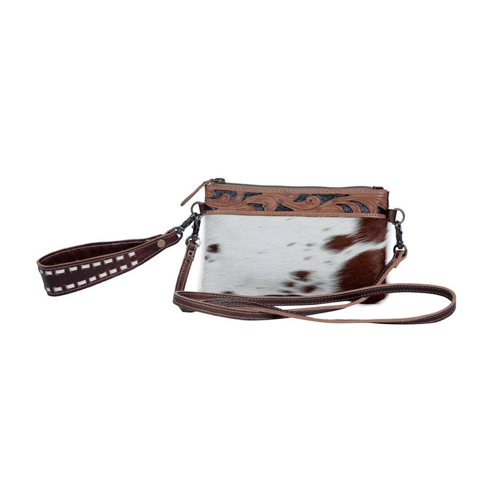 Stylish hairon leather belt bag featuring a brown and white cowhide exterior, hand-tooled detailing, and dual straps.