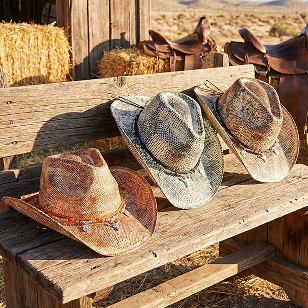 Three handmade vintage cowboy hats displayed on a wooden bench. The hats feature textured wrappings, distinct western charms, and curved brims.