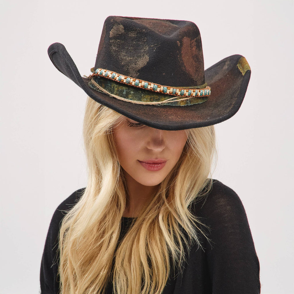 Distressed black cowgirl fedora hat with a shapeable brim and a rustic band, worn slightly tilted on a model's head.