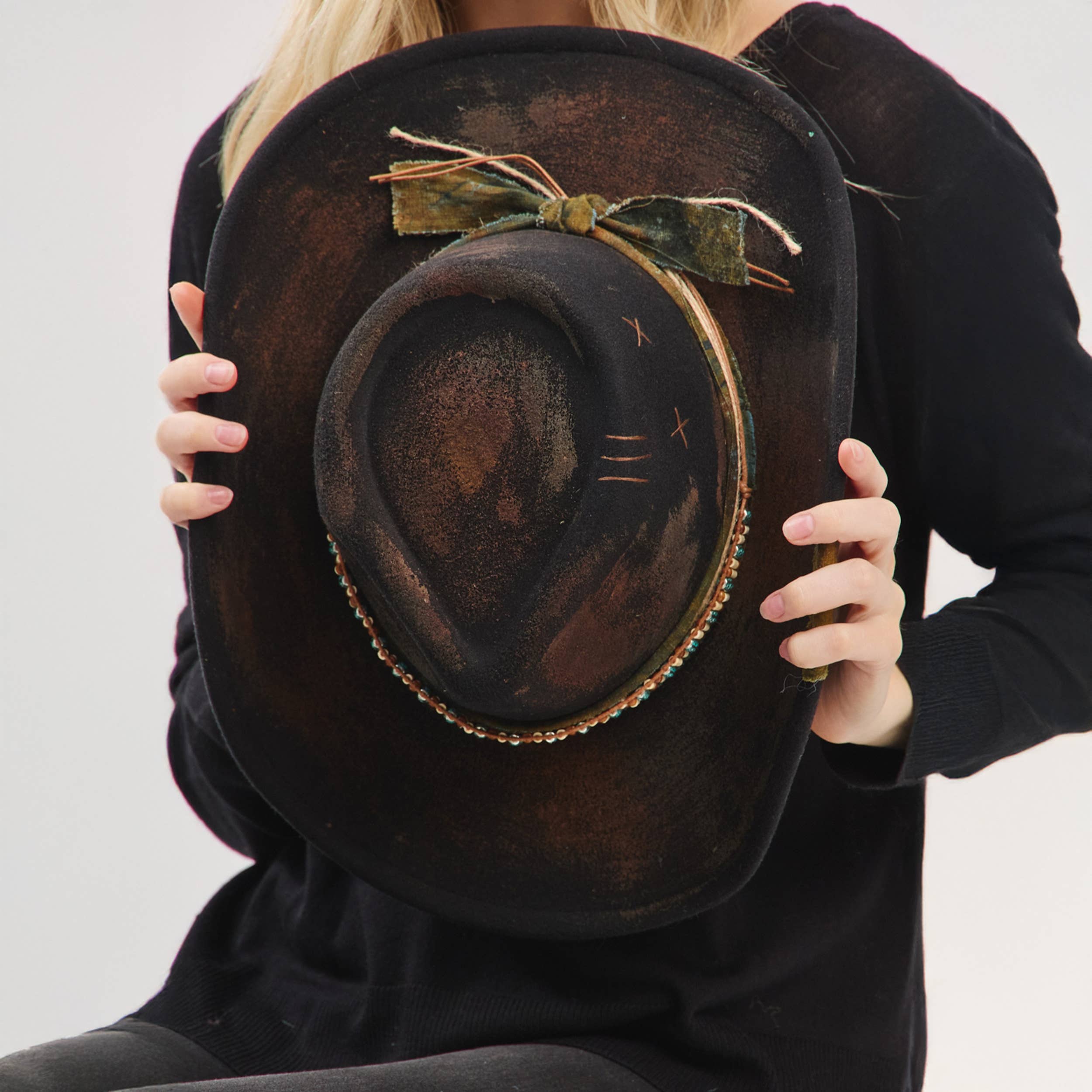 Distressed cowgirl fedora hat with a flexible brim, rustic fabric band, and decorative bow, held by a model.