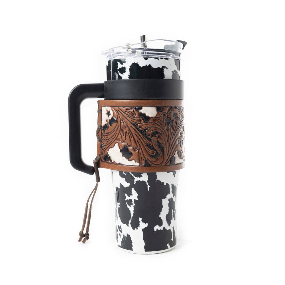 Black and white cowhide print tumbler with chocolate brown leather wrap, ergonomic handle, and spill-resistant lid.