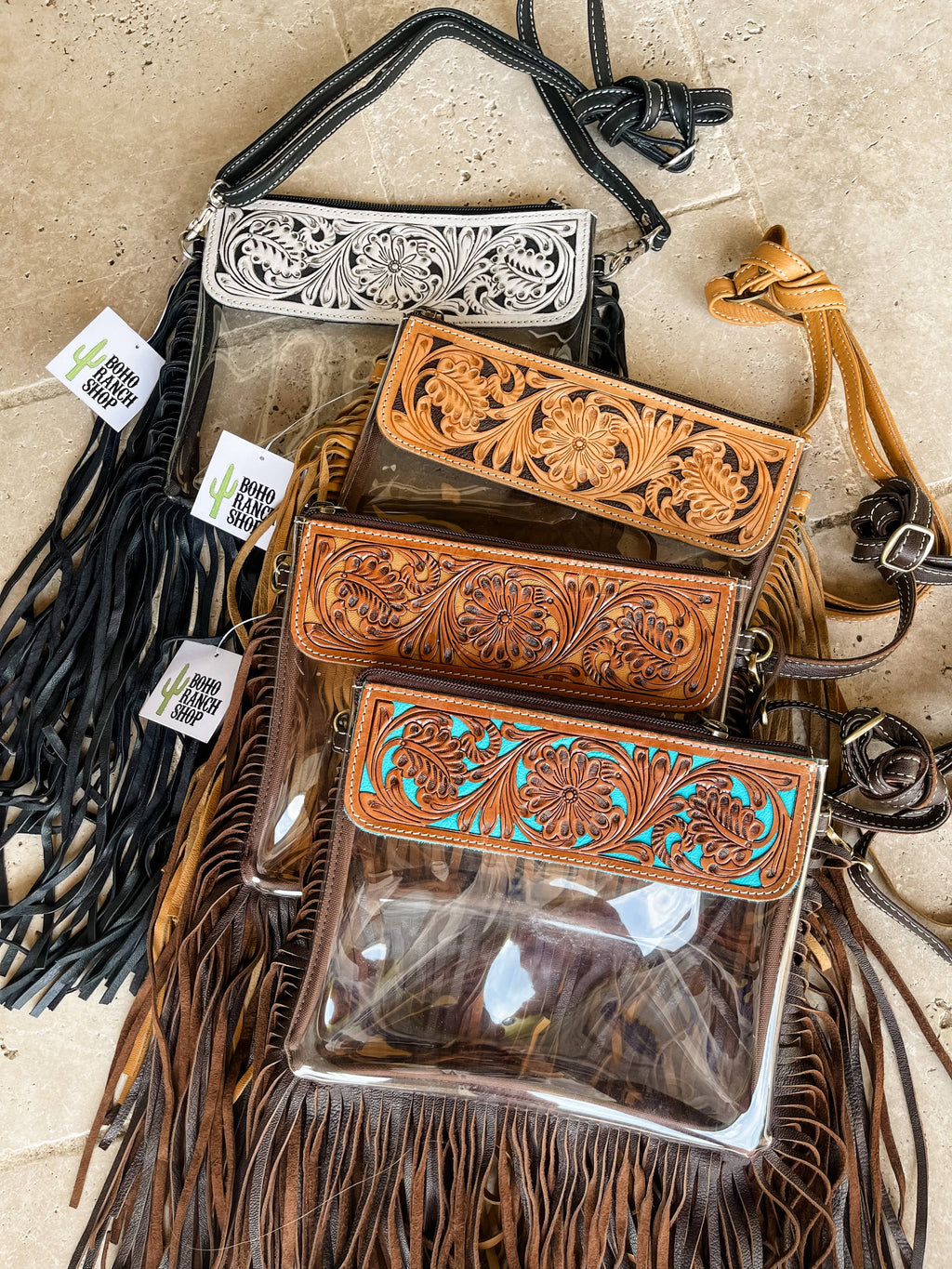 Clear crossbody purses featuring hand-tooled leather designs. Includes black, tan, and brown options with fringe.