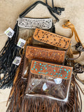 Clear crossbody purses featuring hand-tooled leather designs. Includes black, tan, and brown options with fringe.