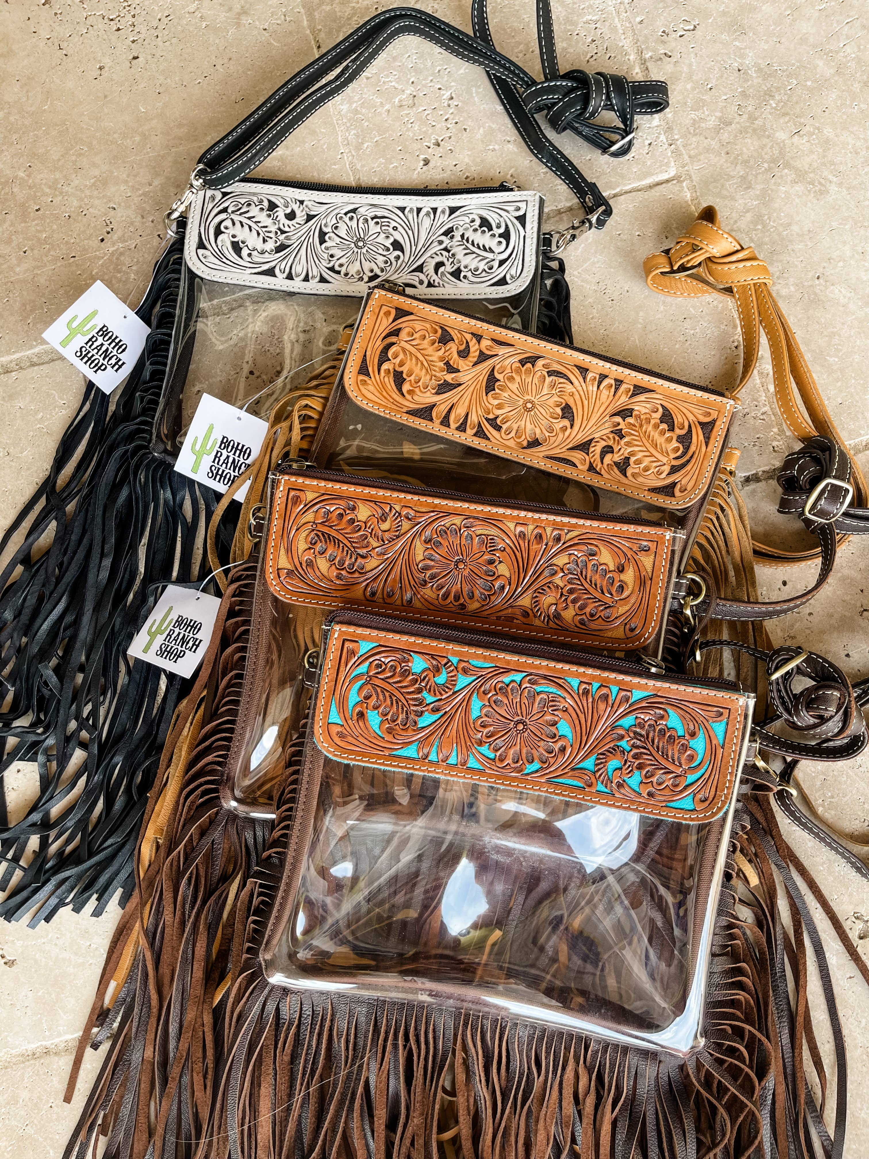 Clear crossbody purses featuring hand-tooled leather designs. Includes black, tan, and brown options with fringe.