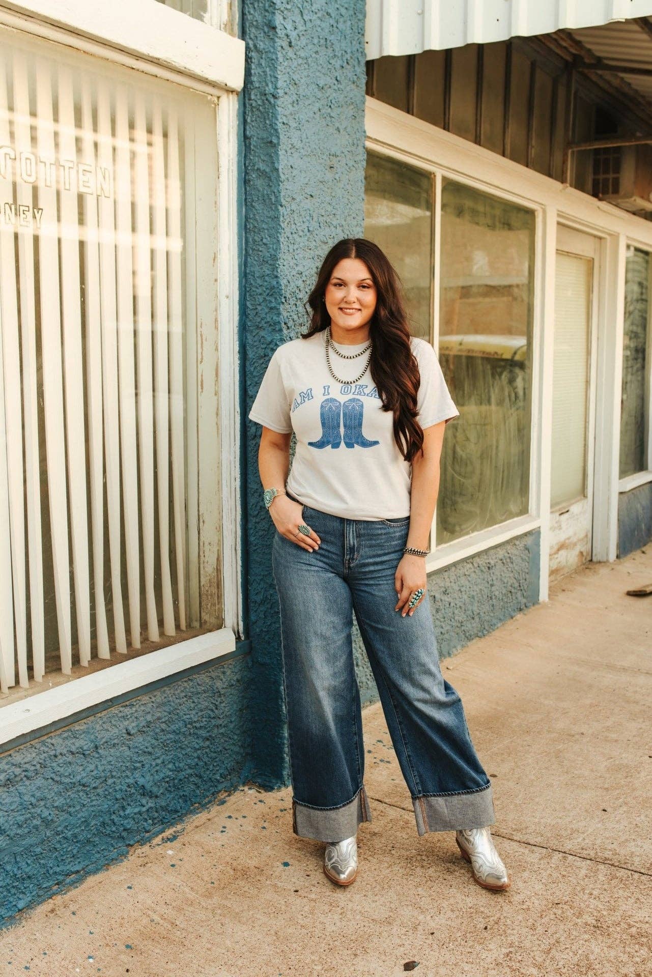 Woman wearing Am I Okay Graphic Tee with blue boots design and cuffed jeans outdoors