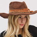 Vintage versatile shapeable cowgirl and fedora hat with feather and distressed fabric band worn by woman