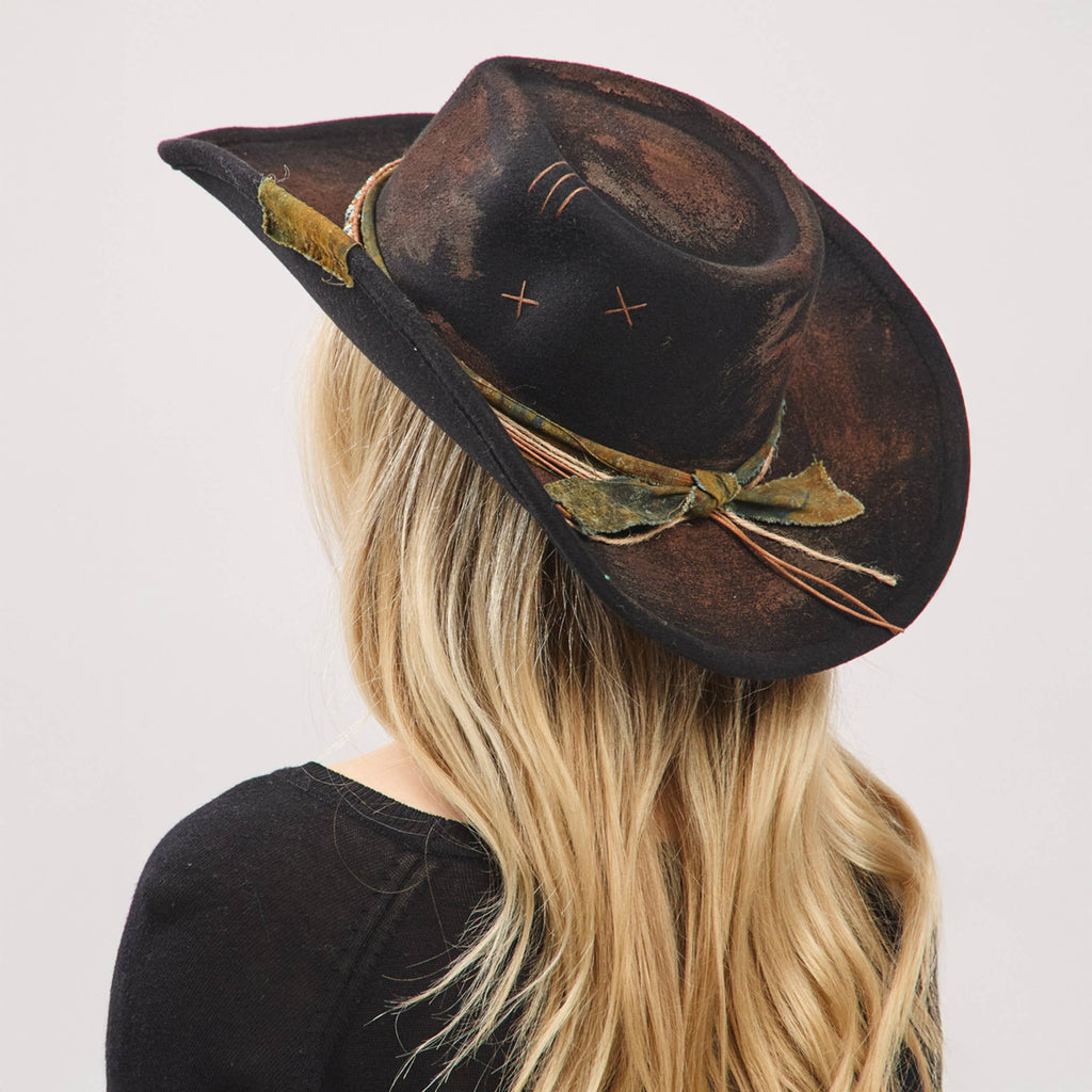 Distressed black cowgirl fedora hat with a flexible brim, featuring a rustic fabric band and bow detail.