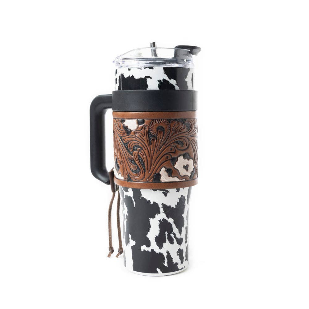 Wide Wyoming Tumbler in black and white with a cowhide print, tooled leather wrap, ergonomic handle, and spill-resistant lid.