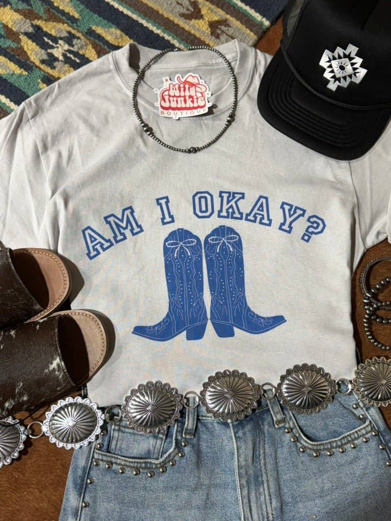 Am I Okay Graphic Tee with blue cowboy boots print, unisex fit, styled with denim shorts, concho belt, black cap, and brown sandals.