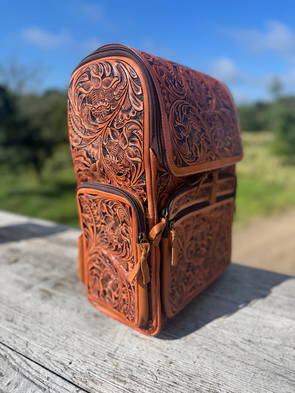 Fully tooled genuine leather backpack with intricate floral designs, featuring multiple zippered pockets and adjustable straps.