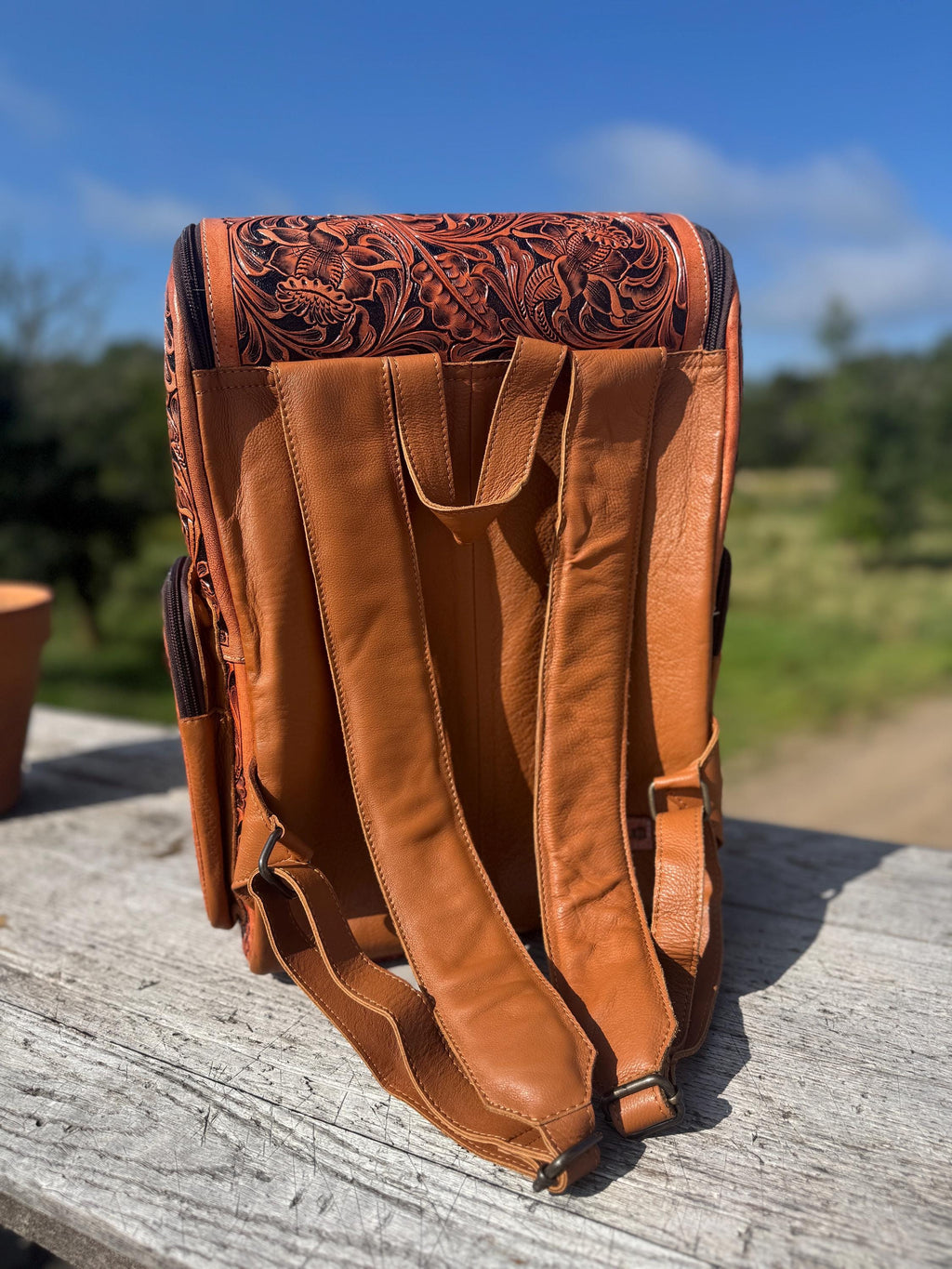 Genuine leather backpack with tooled design, adjustable straps, and various zip pockets in a warm tan color.
