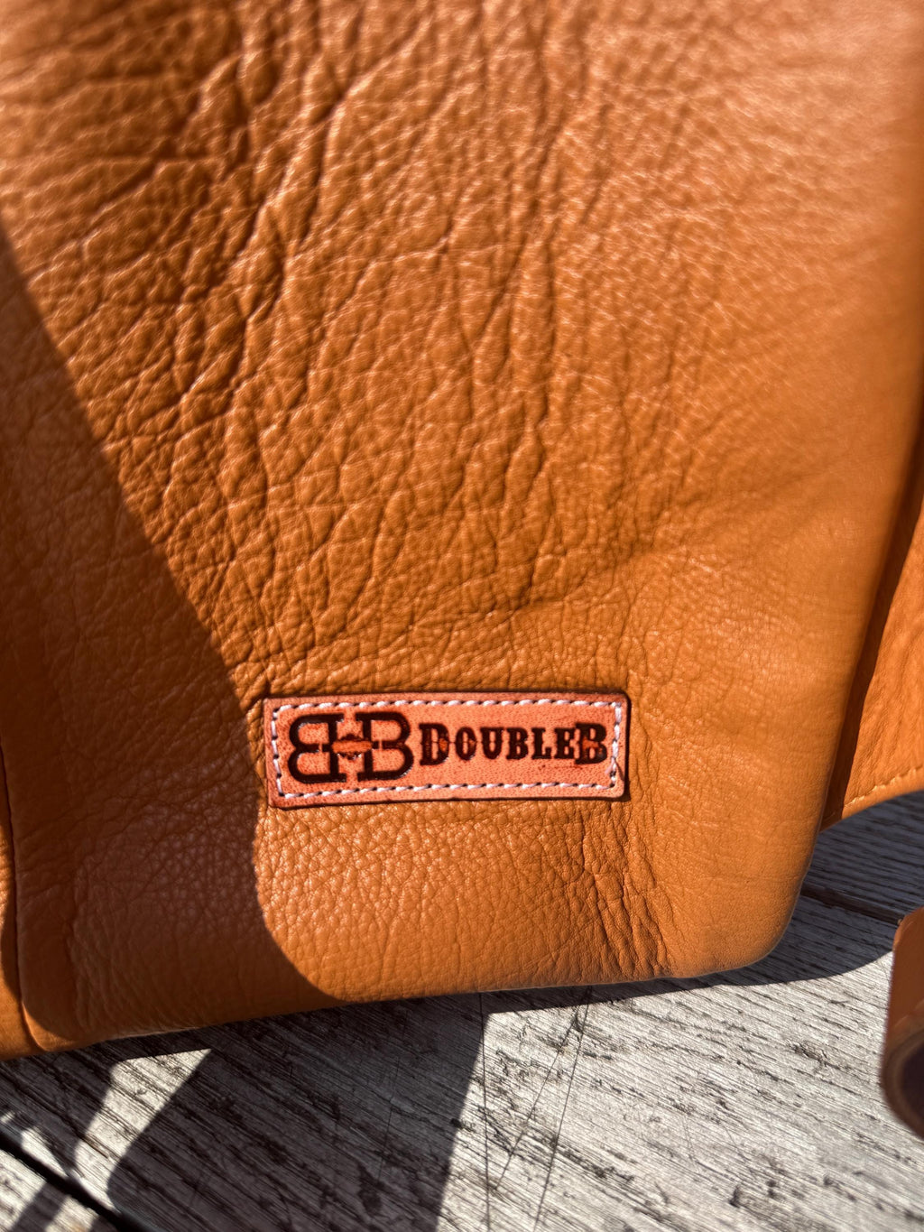 Brown textured leather backpack with Double B logo, showing rich grain and a warm color.