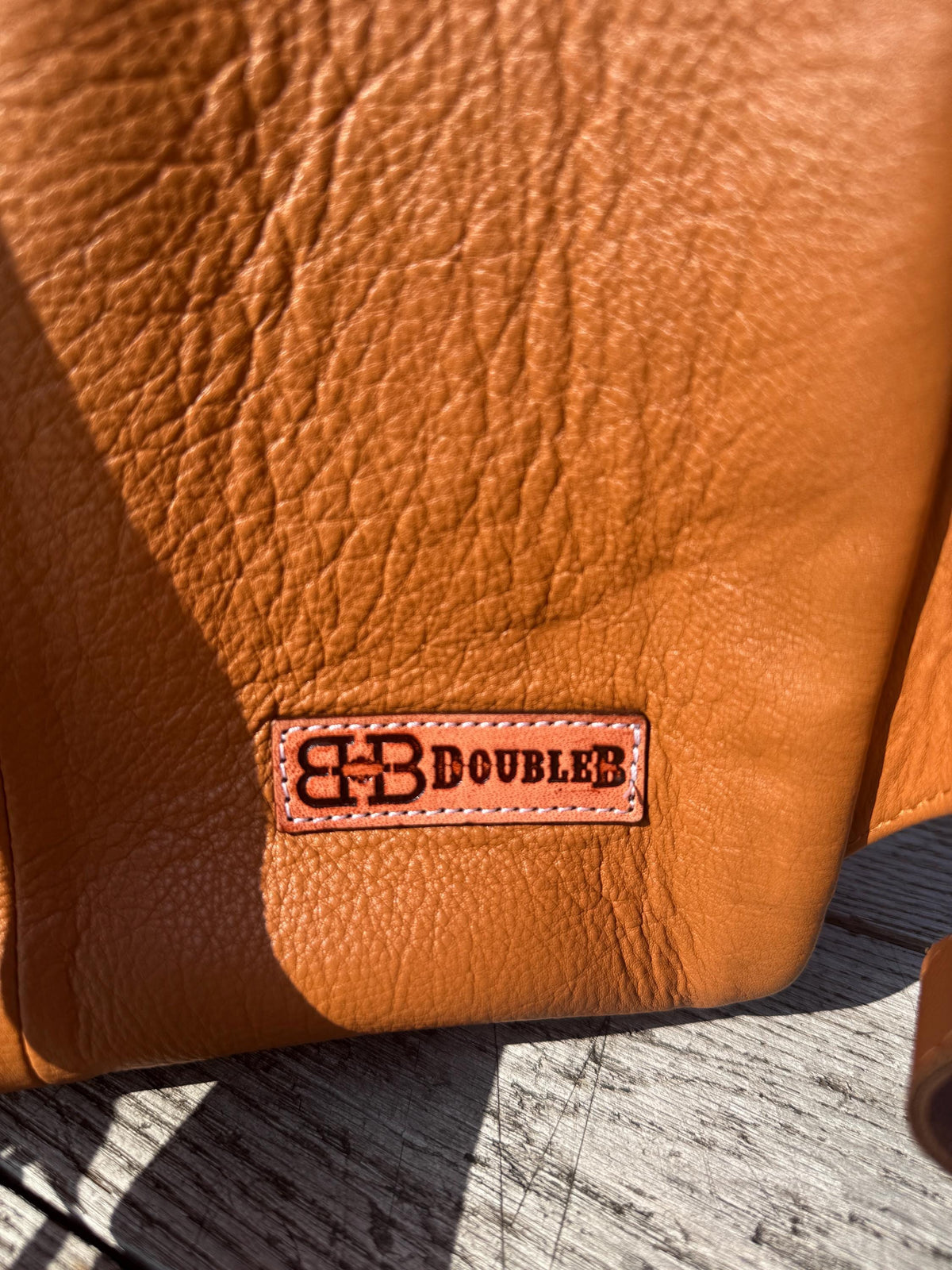 Brown textured leather backpack with Double B logo, showing rich grain and a warm color.
